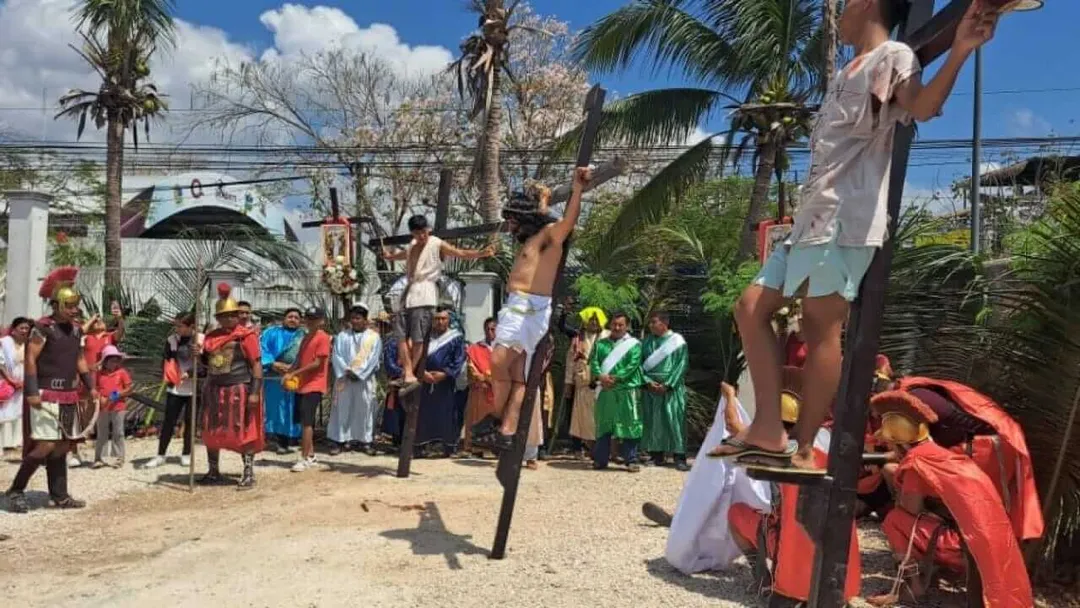 Tulum Walks the Path of Faith in a Powerful Good Friday Procession Participants in religious procession reenactment stand and kneel around figures suspended on wooden crosses in sandy outdoor setting surrounded by palm trees