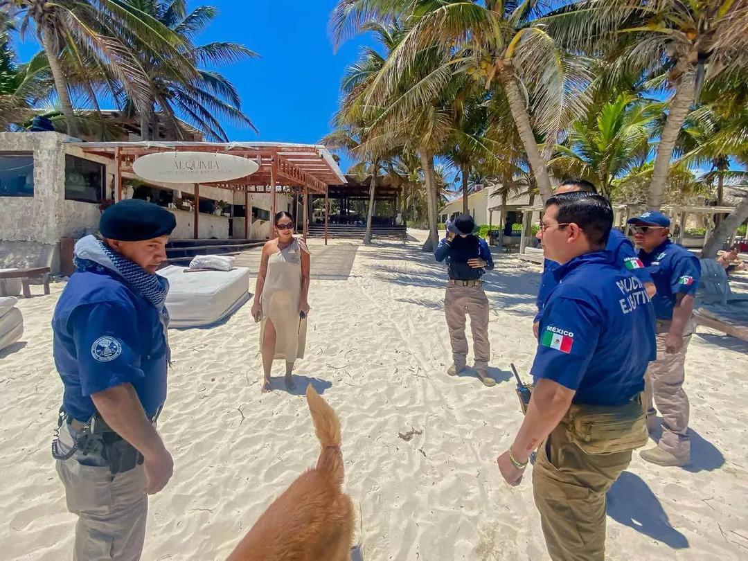 Uniformed officers stand on a sandy beach near palm trees and beachfront buildings during daytime
