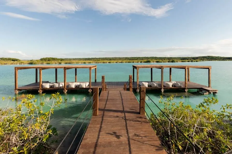 Discover Bacalar: A Yucatan Travel Guide for the Discerning Explorer Wooden dock with covered lounging platforms extends into turquoise water lined with mangrove vegetation under clear sky