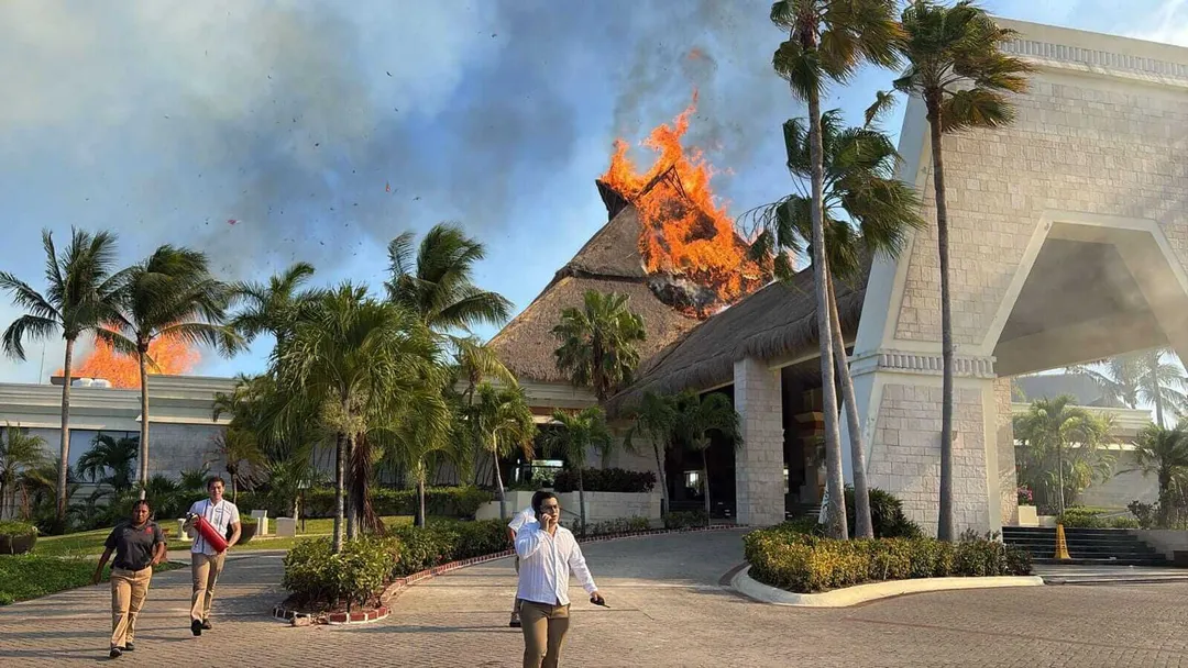 Fire engulfs a thatched-roof structure at a resort as visitors and staff evacuate from the grounds