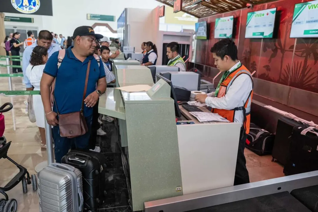 Tulum Tightens Entry Rules Amid National Security Concerns A man in a blue shirt and cap stands at a ticket counter with luggage while an employee in an orange safety vest processes his documents at what appears to be a