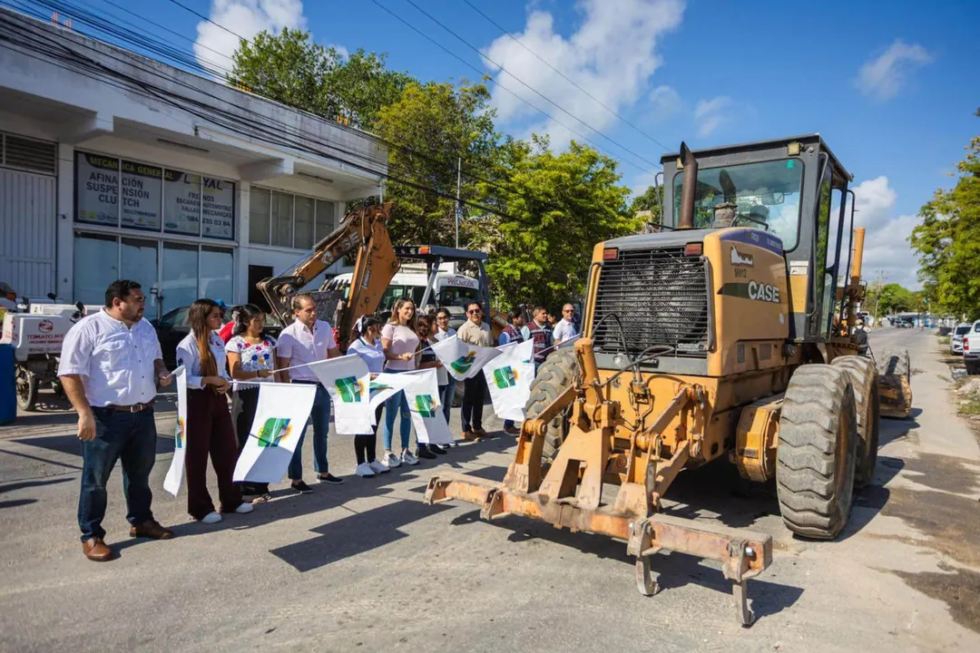 Coba Avenue Rehabilitation Begins in Tulum A group of people holding flags stand in a street next to heavy construction equipment during a road project ceremony