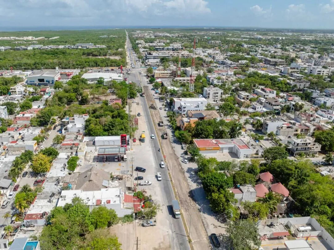 Aerial view of a wide straight road cutting through a sprawling town with buildings, trees, and flat landscape extending to the horizon
