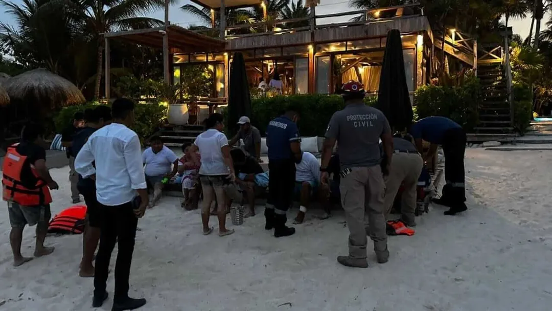 Civil protection personnel and residents gather on a beach near an illuminated building with palm trees visible in the background