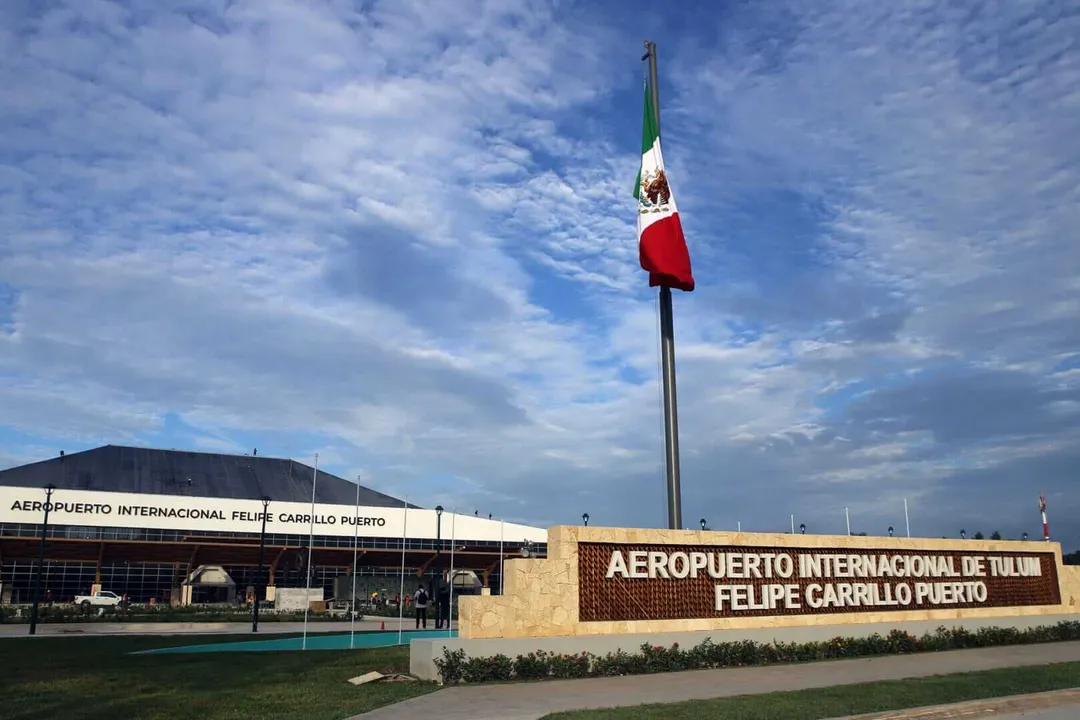 Tulum Airport Gears Up for 2026 World Cup Boost in Mexican Caribbean Mexican flag flies on a tall pole in front of an airport terminal building with signage reading "Aeropuerto Internacional de Tulum Felipe Carrillo Puerto