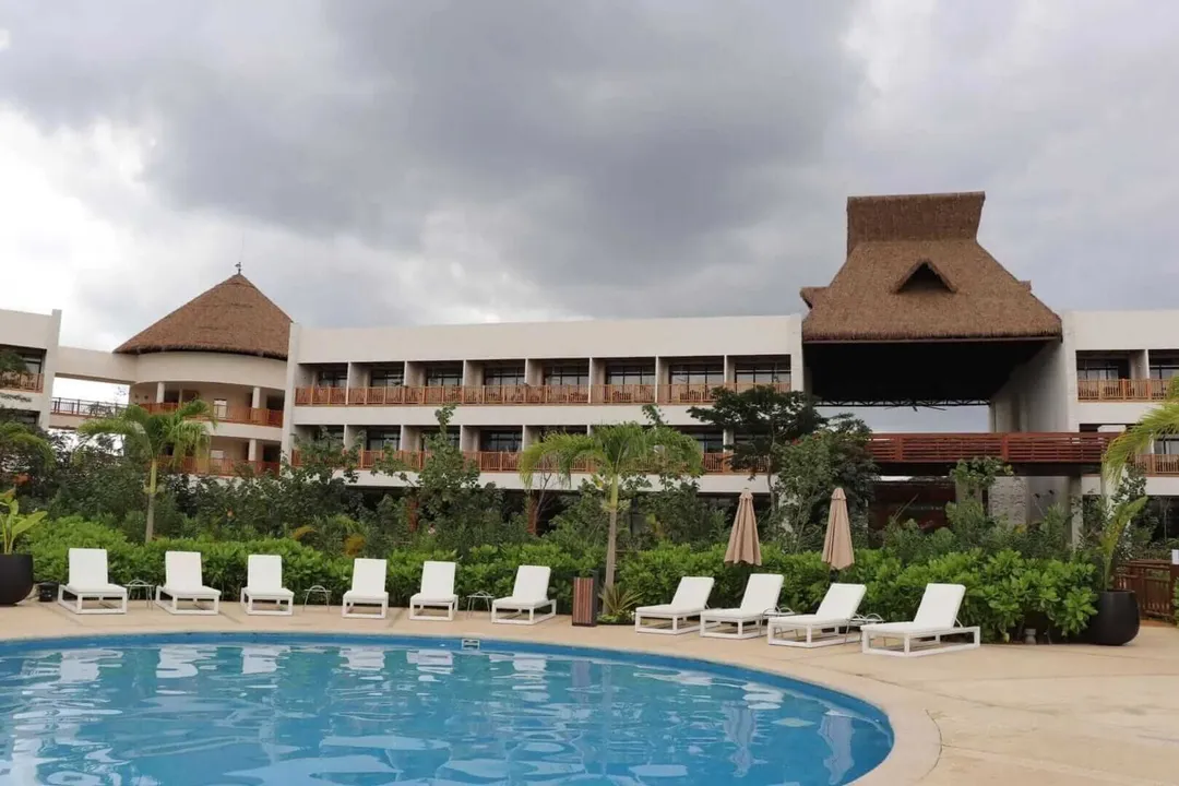 Comparing Maya Train hotels Prices with Private Riviera Resorts Resort with thatched-roof structures overlooks a curved swimming pool lined with white lounge chairs and umbrellas under cloudy skies