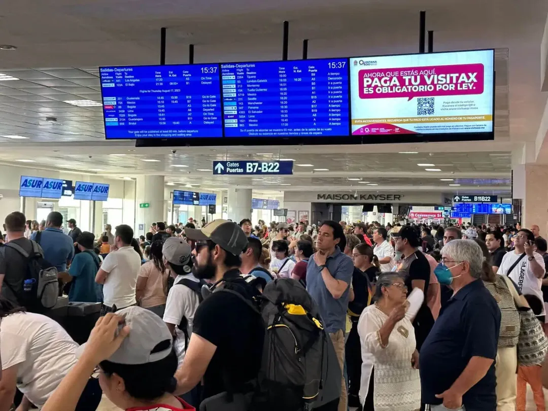 Crowd of travelers gathered at airport gate area beneath departure boards and signage in Spanish