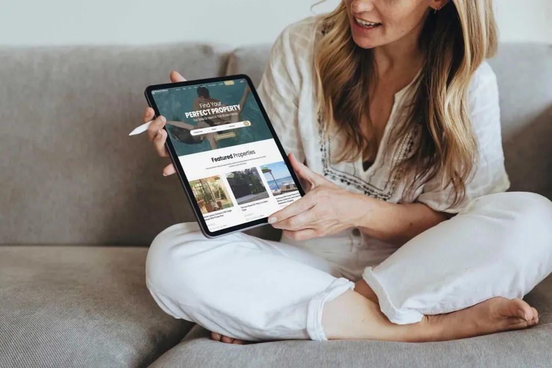 One Woman’s Journey Through the Riviera Maya Real Estate Maze Woman sitting on a couch holds a tablet displaying a real estate website with property listings