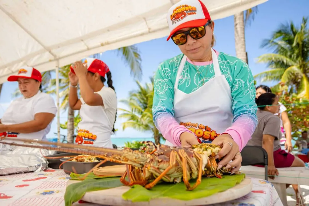 Woman in red cap and sunglasses prepares food under a tent with palm trees visible in the background at an outdoor cooking event