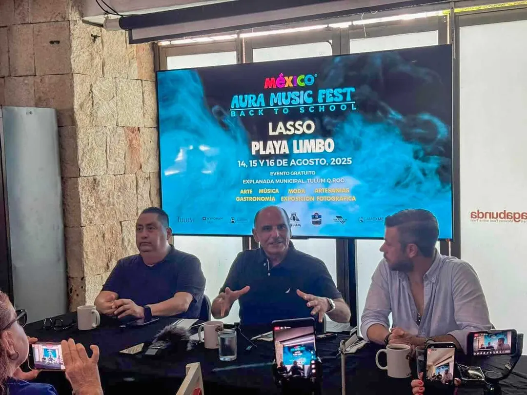 New Tulum music festival Aura Music Fest aims to attract visitors in August Three men sit at a panel table with microphones and water bottles, facing an audience holding phones to record, with a large screen behind them displaying infor