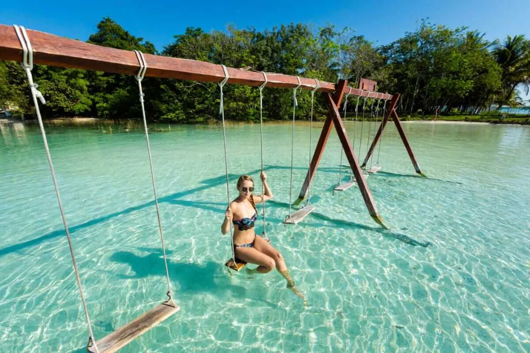 Woman on a swing in shallow turquoise lagoon water surrounded by mangroves and wooden swing structures