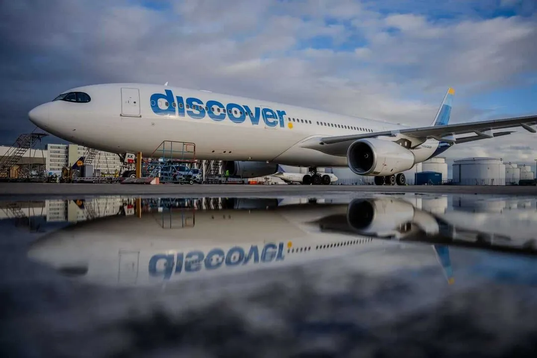 Commercial aircraft with "discover" branding parked at an airport terminal, reflected in standing water on the tarmac