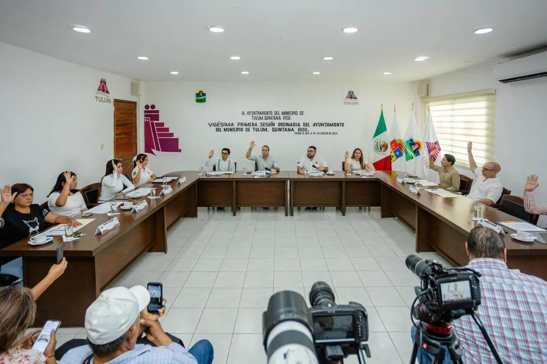 Municipal officials and media representatives attend a government meeting in a council chamber with Mexican flags displayed