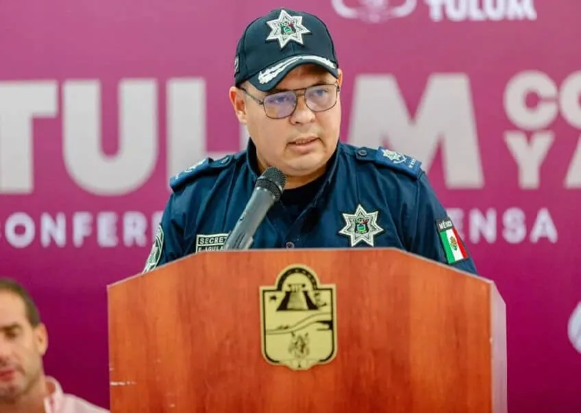 Law enforcement official in uniform speaks at a wooden podium during a press conference with a pink banner behind him