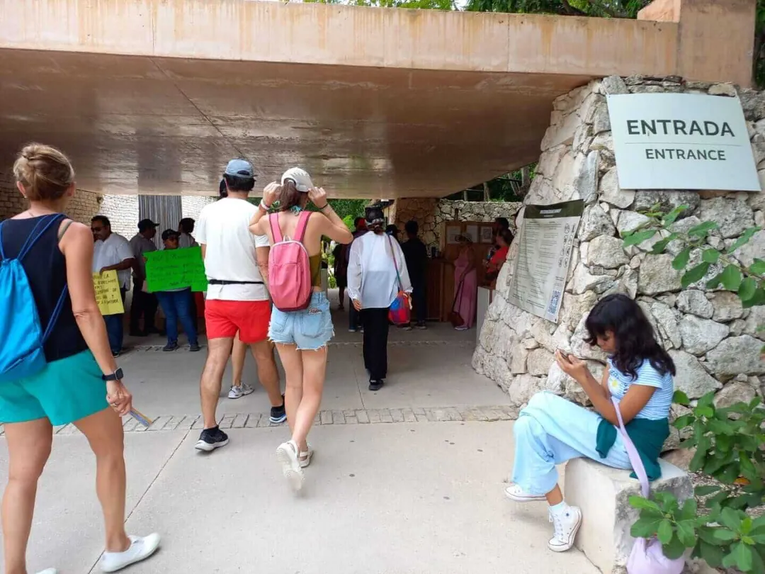 Visitors queue at an entrance sign beneath a concrete overhang at what appears to be an archaeological site