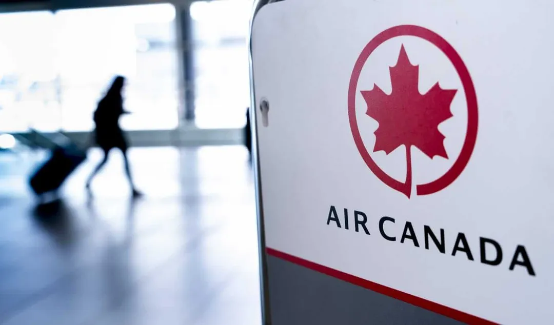 Air Canada logo displayed at an airport terminal with a traveler walking in the background