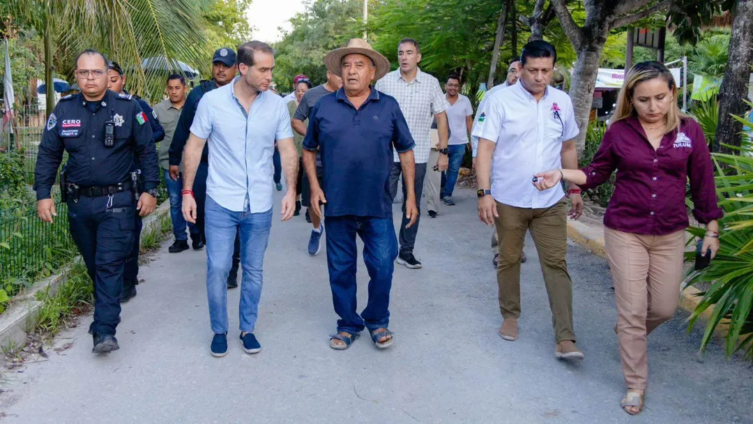 A group of officials and residents walk together down a tree-lined path in a tropical setting