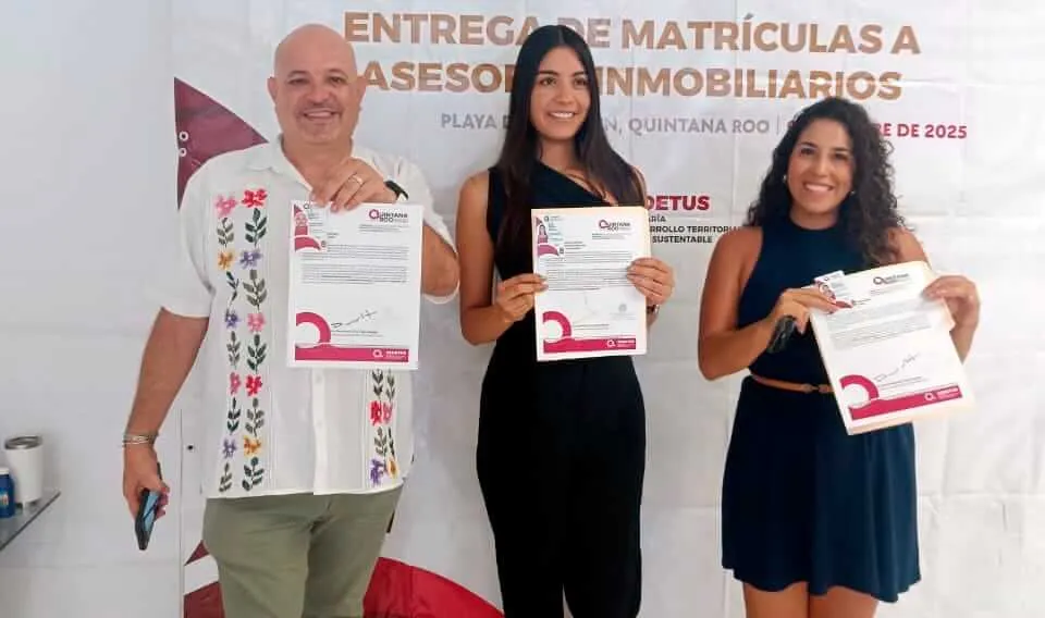 Three people hold certificates at a credential presentation event, with a banner behind them referencing real estate agent certification in Quintana Roo