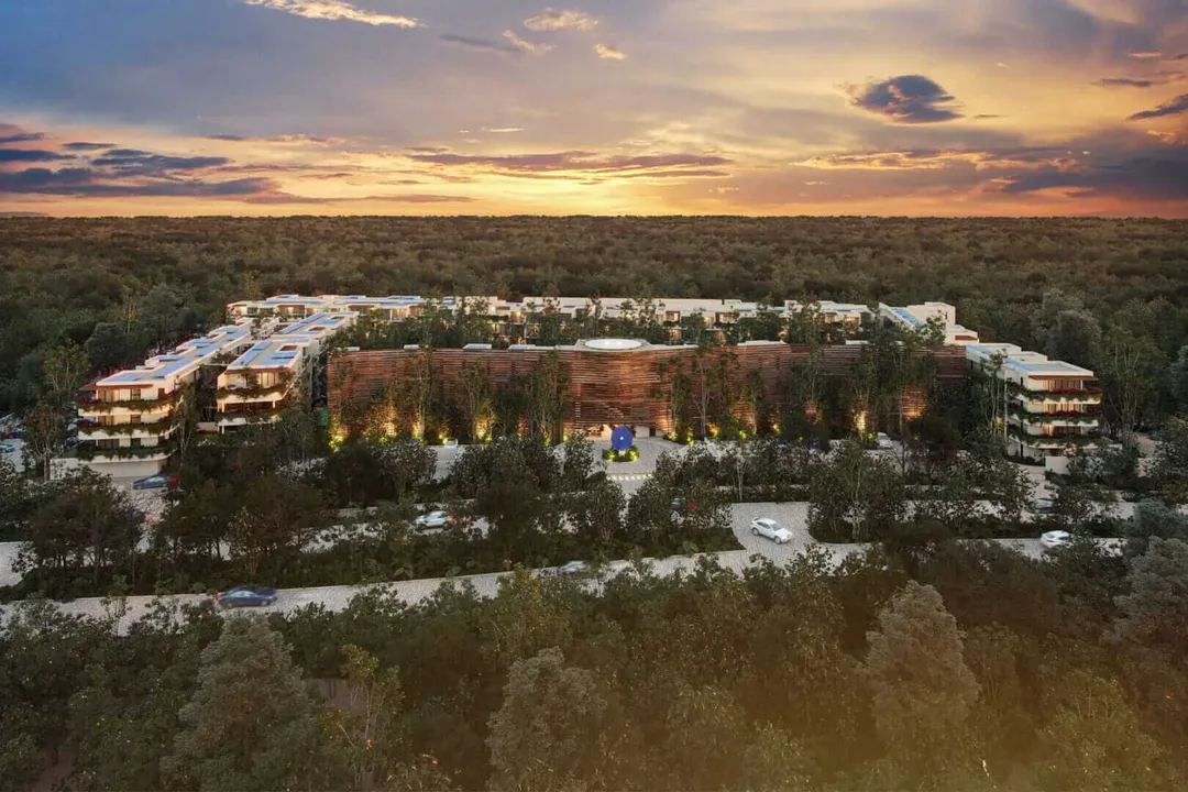 Own a Piece of Tulum’s Future at 101 Park Large modern residential complex with curved architecture nestled among trees in a forested landscape at sunset