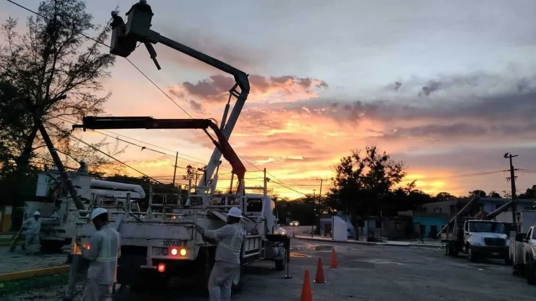 Tulum Blackouts Explained as CFE Upgrades La Veleta Grid Utility workers operate an aerial lift truck on a residential street at sunset while power lines and equipment are visible in the background