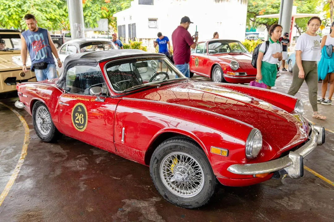 Red convertible sports car with number 26 displayed at an outdoor classic car show with spectators and other vintage vehicles nearby