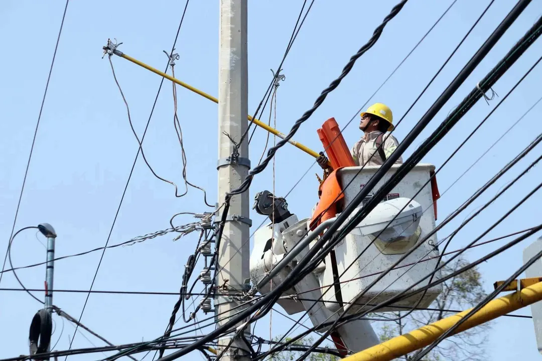 Utility worker in a bucket lift repairs electrical lines and equipment on a concrete pole against a clear sky