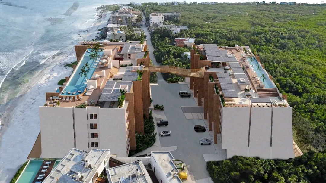 Aerial view of a large residential complex with swimming pools and parking areas built on a coastal hillside between beach and dense vegetation