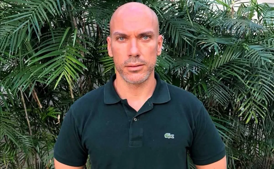Man in dark polo shirt standing in front of dense tropical foliage