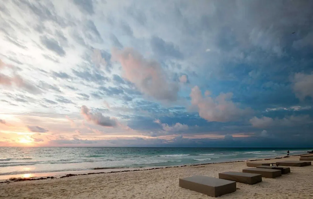 Beach with concrete platforms in foreground and person swimming in the water at sunset