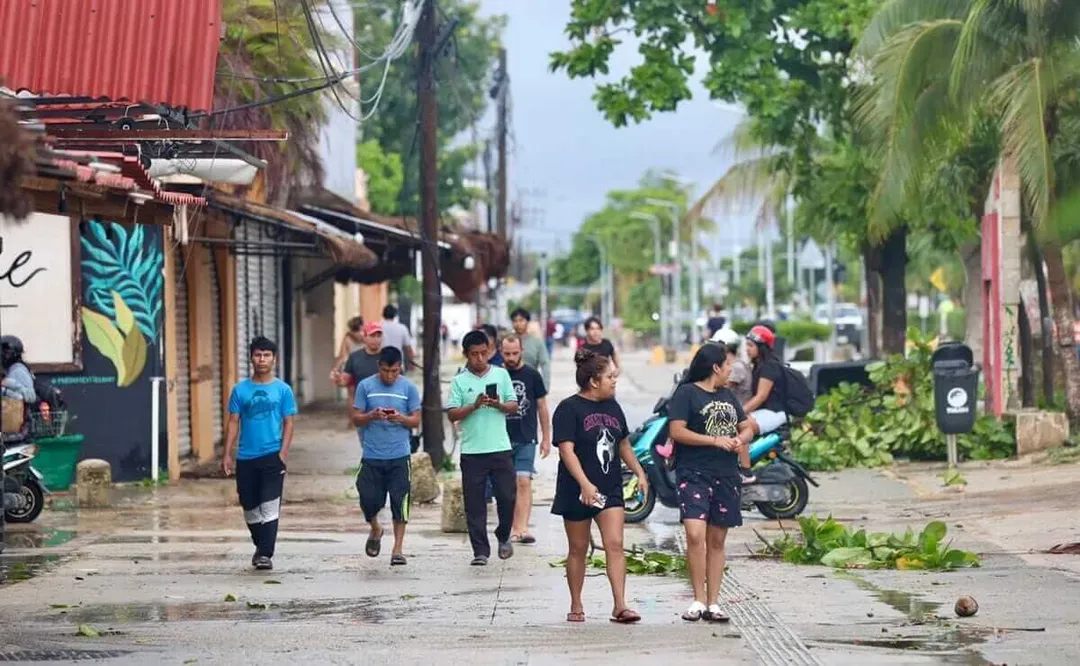 Can Tulum grow without pushing locals out? A group of children and young people run and play on a wet street lined with palm trees and colorful buildings