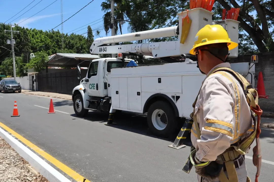 Utility worker in yellow hard hat and safety harness stands near a white service truck with aerial lift parked on a residential street