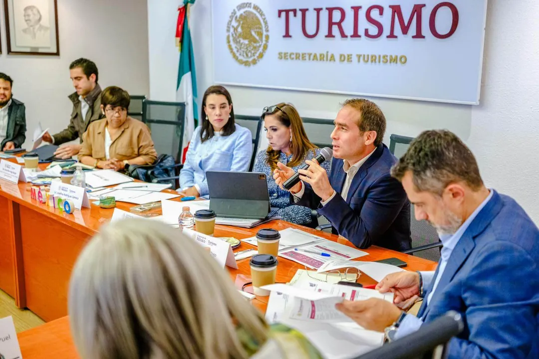 What is Tulum doing to win back travelers this winter? Several people sit at an orange table during a meeting at a tourism office, with a man in a blue jacket speaking while others listen and take notes