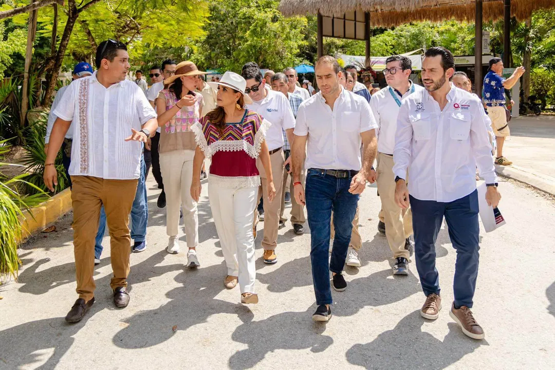 New branding, better access, and a Master Plan for Tulum revealed A group of visitors and officials walk together along a paved pathway surrounded by tropical vegetation and thatched structures