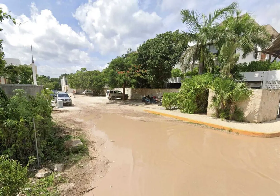 La Veleta’s residents feel abandoned as Tulum expands A residential street flooded with muddy water, lined with palm trees and concrete buildings under a partly cloudy sky