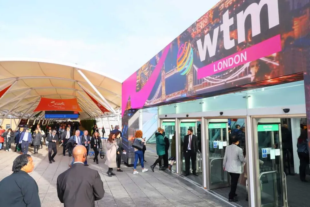 Attendees walk through an outdoor venue with a large colorful banner displaying "WEND" and "LONDON" at what appears to be a travel trade show