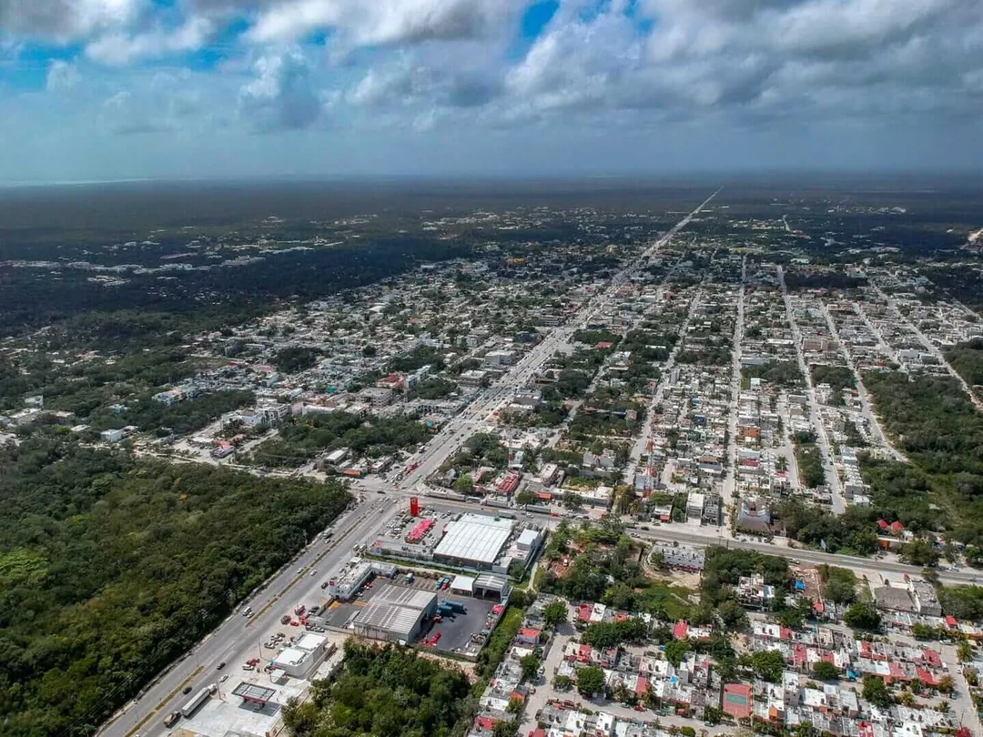 Tulum faces oversupply as vacation rentals outpace demand Aerial view of a sprawling residential and commercial area with a divided highway running through it, surrounded by dense forest
