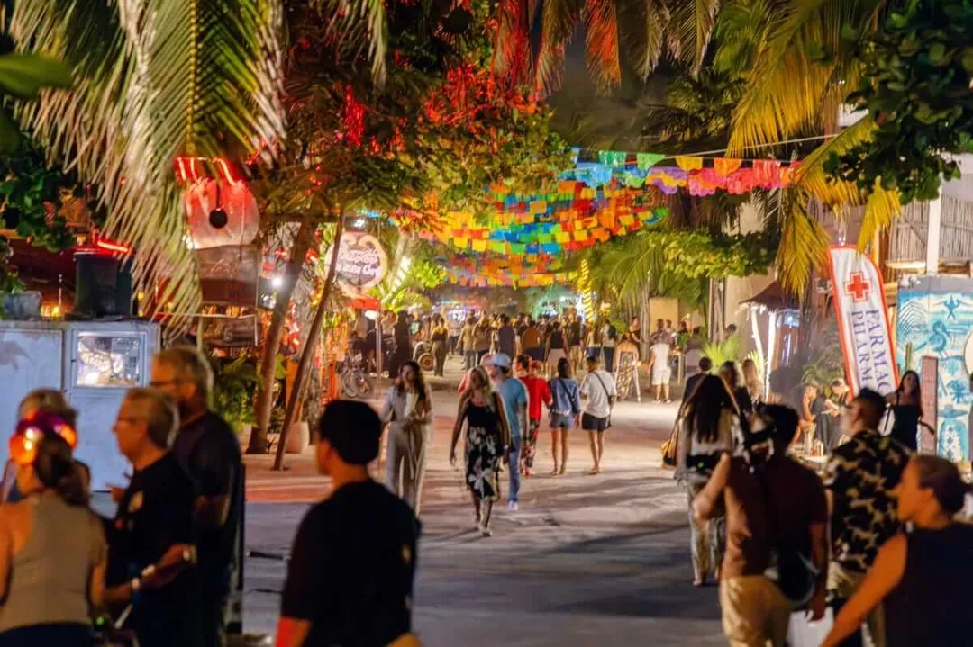Tulum confirms Pueblo Mágico status as renewal process advances Crowds walk through a palm-lined street decorated with colorful paper banners and neon signs at night