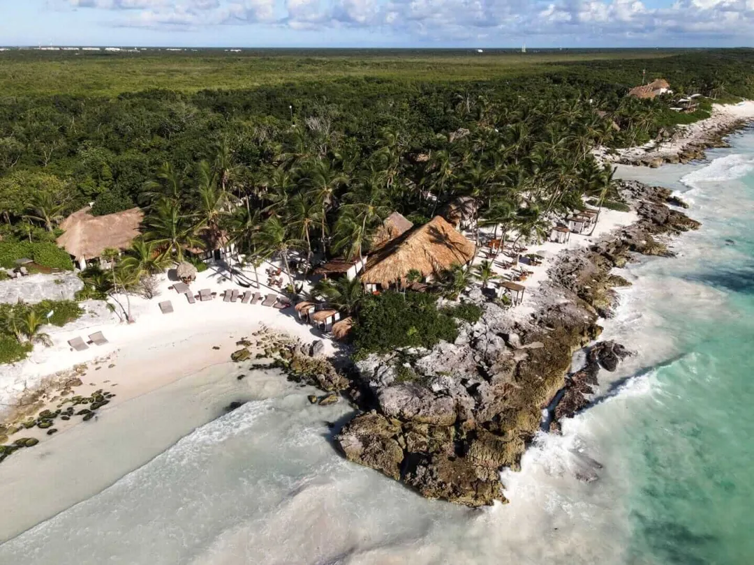 Mixed signals from Profeco and Diamante K deepen local concern Aerial view of a coastal settlement with thatched-roof structures nestled between dense tropical vegetation and a turquoise ocean shoreline with rocky outcroppi