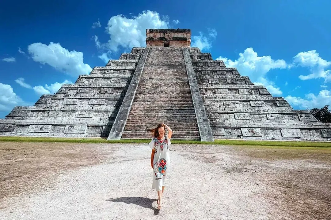 Chichén Itzá leads again while Tulum struggles to rebound Woman in white dress walking toward a large stepped pyramid under blue sky with white clouds