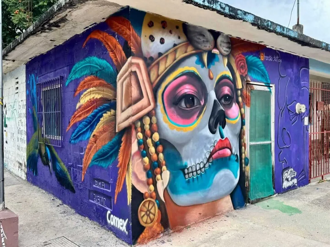 A corner building decorated with colorful street art featuring stylized faces with skull-like makeup and vibrant feathers against a purple background