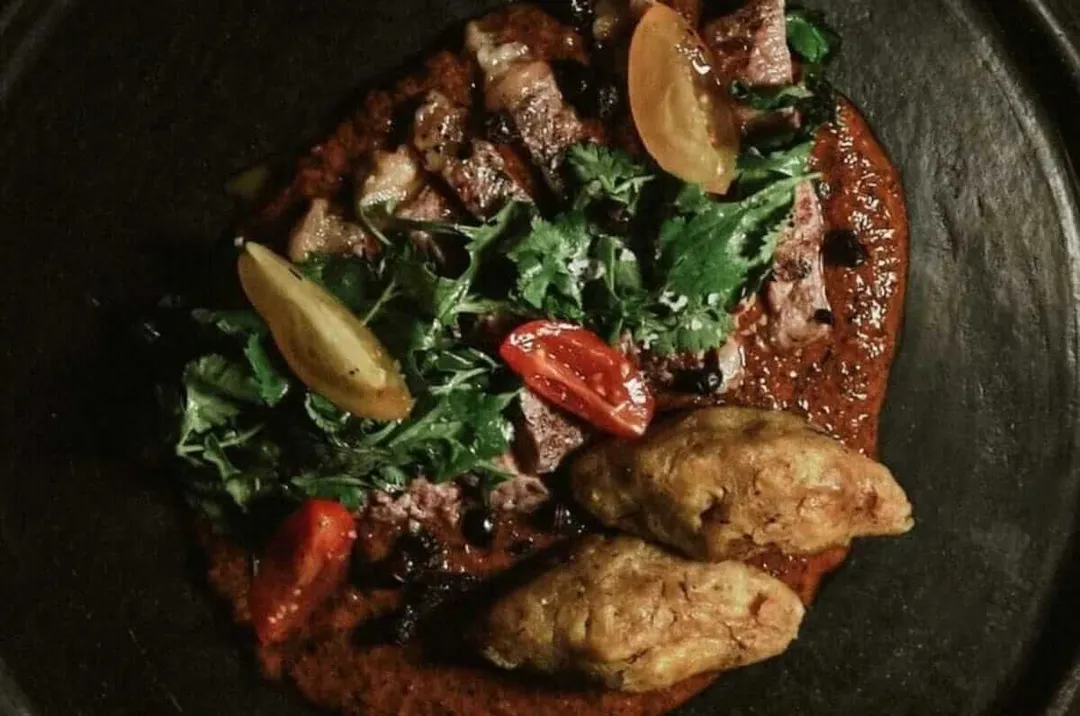 Mole traditions take center stage during Tulum’s second FGMT Seared steak topped with fresh herbs, sliced potatoes, and red peppers on a dark plate