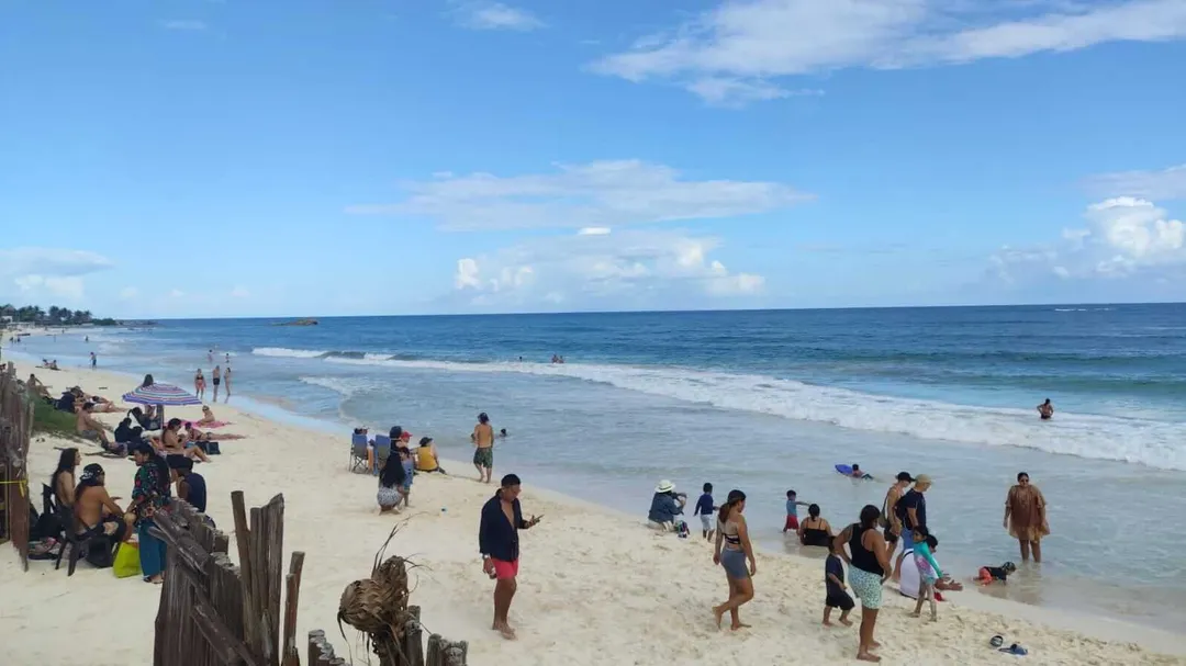 Beachgoers swim and relax on sand while waves roll onto shore under a partly cloudy sky