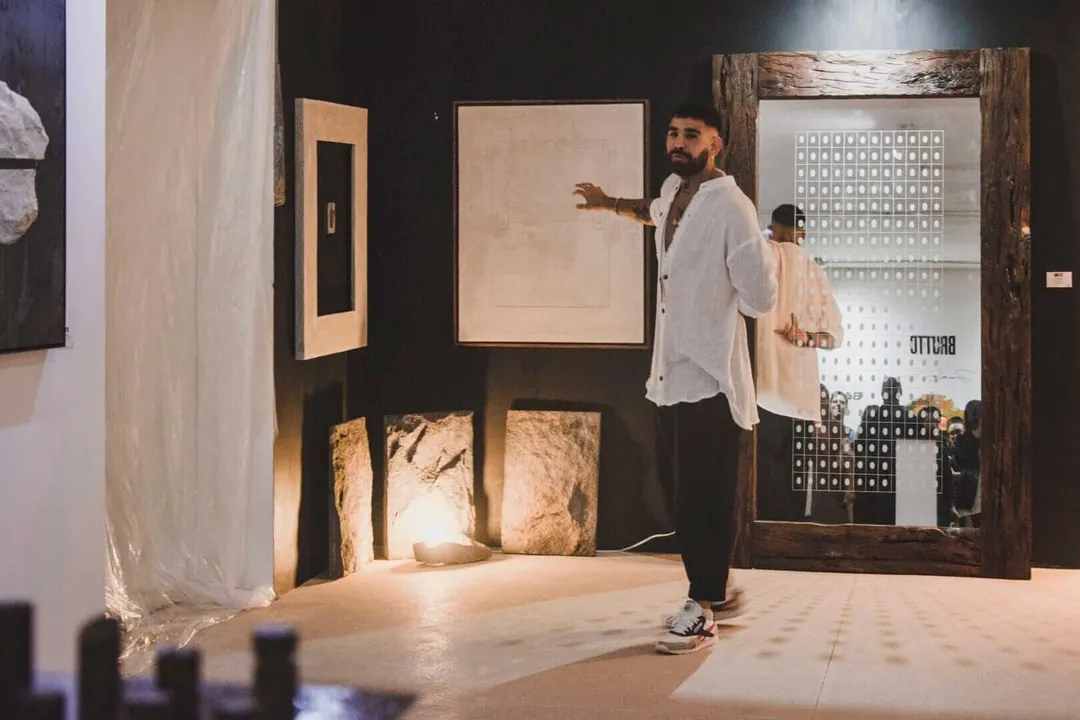 Man gesturing toward artwork displayed on dark walls inside a gallery or exhibition space