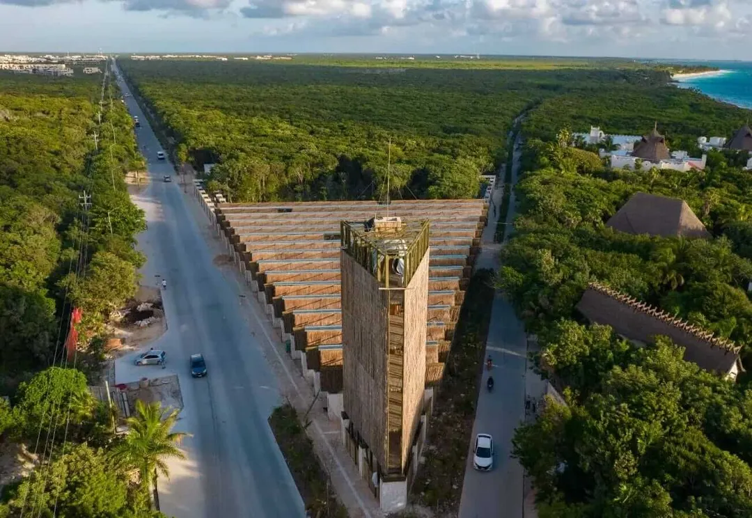 Aerial view of a pyramid structure surrounded by forest with roads, residential buildings, and coastal waters visible in the distance
