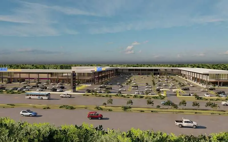 Tulum Plans New Mixed-Use Center With First Local Movie Theater in 2026 Aerial view of a large retail center under construction with a parking lot, surrounding vehicles, and flat landscape with trees in the distance