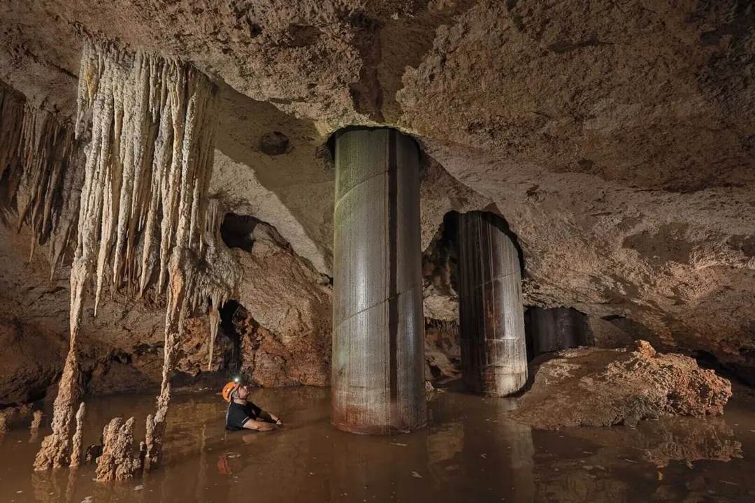 Sélvame MX considers new lawsuit over Tren Maya Route 5 South damage Person wading through shallow water inside a cave with stalactites and support columns
