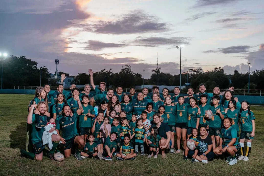 Tulum Rugby Club chases historic back-to-back national title Large group of rugby players and staff in teal uniforms posing together on a grass field at dusk under floodlights