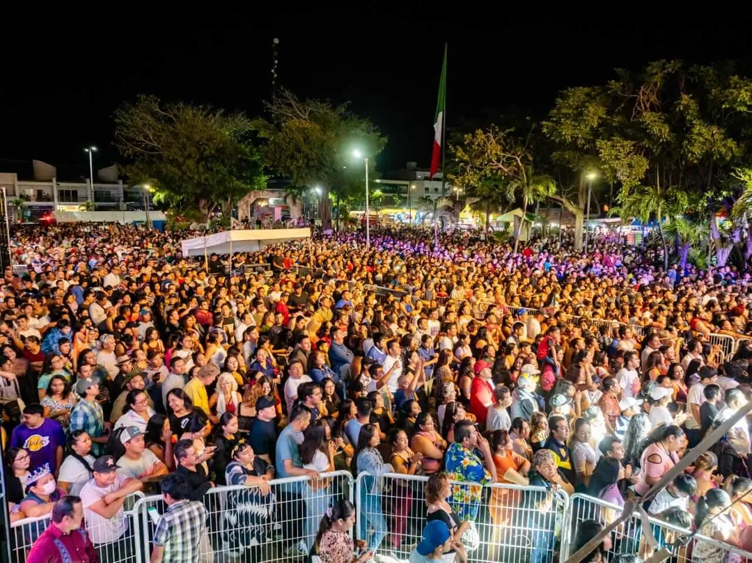 Tulum Urges Heightened Precaution Against Measles During Carnival Festivities Large crowd gathered at night in an open plaza with metal barriers, surrounded by trees and lit by street lights, with a flag visible in the background