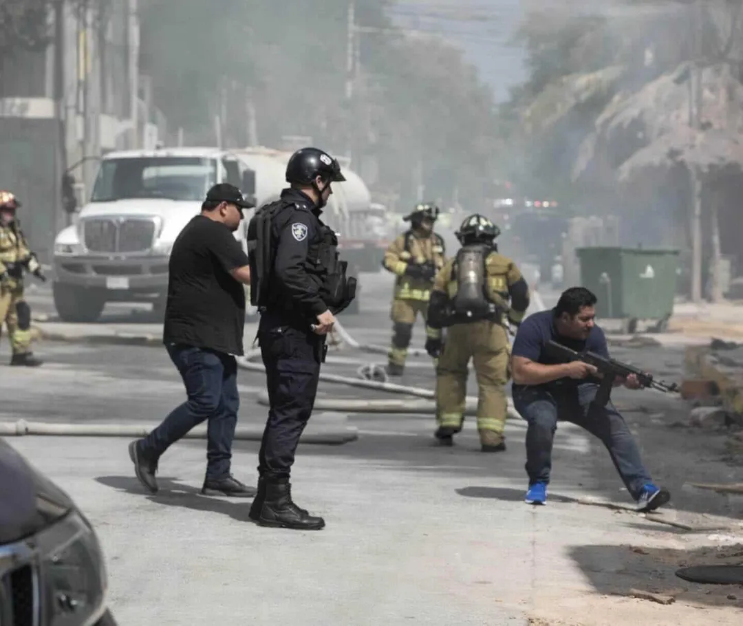 Police and firefighters work on a smoke-filled street with vehicles and emergency responders present