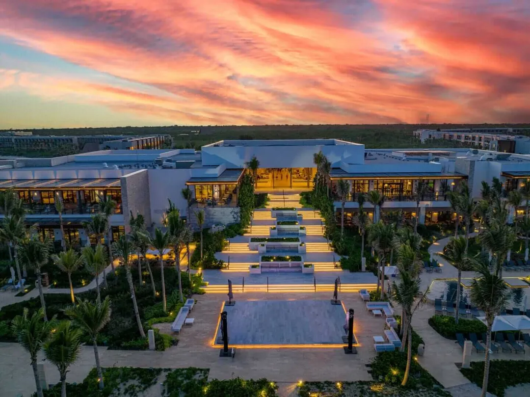 Invited by Hilton Tulum, a stay that allowed us to disconnect Modern resort with illuminated courtyard and palm trees at dusk, surrounded by white buildings overlooking flat landscape